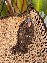 Load image into Gallery viewer, Close-up of a woven bag with a colorful tag against a natural background