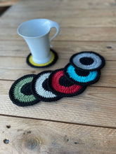 Load image into Gallery viewer, Set of colorful crocheted coasters on a wooden surface with a white mug.