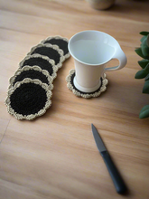 Load image into Gallery viewer, Set of black and beige coasters with a white mug on a wooden surface.
