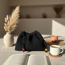 Load image into Gallery viewer, Black knitted pouch with colorful drawstrings on a stone surface