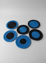 Load image into Gallery viewer, Set of blue and black crocheted coasters with a white mug on a wooden surface.