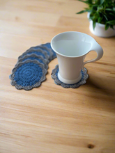 Load image into Gallery viewer, White mug on blue crocheted coasters on a wooden surface with a plant in the background