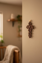 Load image into Gallery viewer, A small crocheted brown cross charm with a light beige hanging loop, hanged on the wall