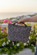 Load image into Gallery viewer, Person holding a textured handbag with a blurred outdoor background
