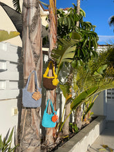 Load image into Gallery viewer, Colorful knitted items on a palm tree with a building and blue sky in the background