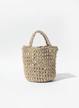 Load image into Gallery viewer, Woven handbag against a neutral wall with plant shadows