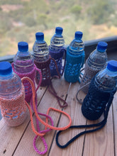Load image into Gallery viewer, Set of water bottles with colorful knitted covers on a wooden surface with a scenic background.