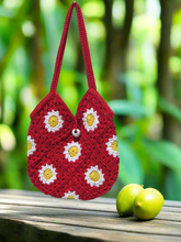 Load image into Gallery viewer, Red crochet bag with white and yellow flower patterns on a wooden surface with green apples and a blurred natural background.