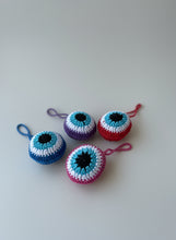 Load image into Gallery viewer, Four crocheted eye-shaped keychains on a wooden surface