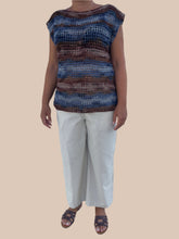 Load image into Gallery viewer, Person wearing a crocheted top with a striped pattern and white pants against a light wooden panel background.