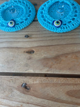 Load image into Gallery viewer, Two blue crocheted coasters with decorative elements on a wooden surface.