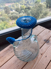 Load image into Gallery viewer, A water jug with a blue and gray crochet cover on a wooden surface