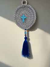 Load image into Gallery viewer, Crocheted circular ornament with blue tassel and cross on a neutral background