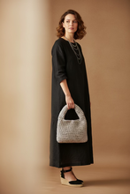 Load image into Gallery viewer, A handmade crochet handbag with a single integrated handle, crafted from chunky light gray and beige yarn, resting on a neutral fabric surface against a plain off-white wall.