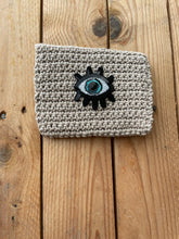Load image into Gallery viewer, Knitted pouch with an evil eye design on a wooden surface