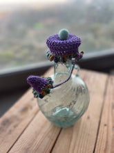 Load image into Gallery viewer, Glass bottle with a purple crochet top on a wooden surface