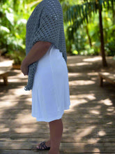 Load image into Gallery viewer, Person wearing a blue knitted shawl over a white dress in a tropical setting