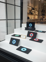 Load image into Gallery viewer, Black pouches with colorful evil eye charms in shop vitrine