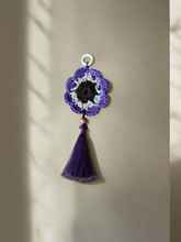 Load image into Gallery viewer, Purple crocheted flower ornament with a tassel on a beige background
