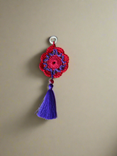 Load image into Gallery viewer, Crocheted flower ornament with a purple tassel on a beige background