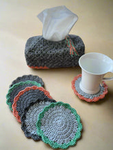 Load image into Gallery viewer, Set of crocheted coasters on a wooden surface with a tissue box and cup.

