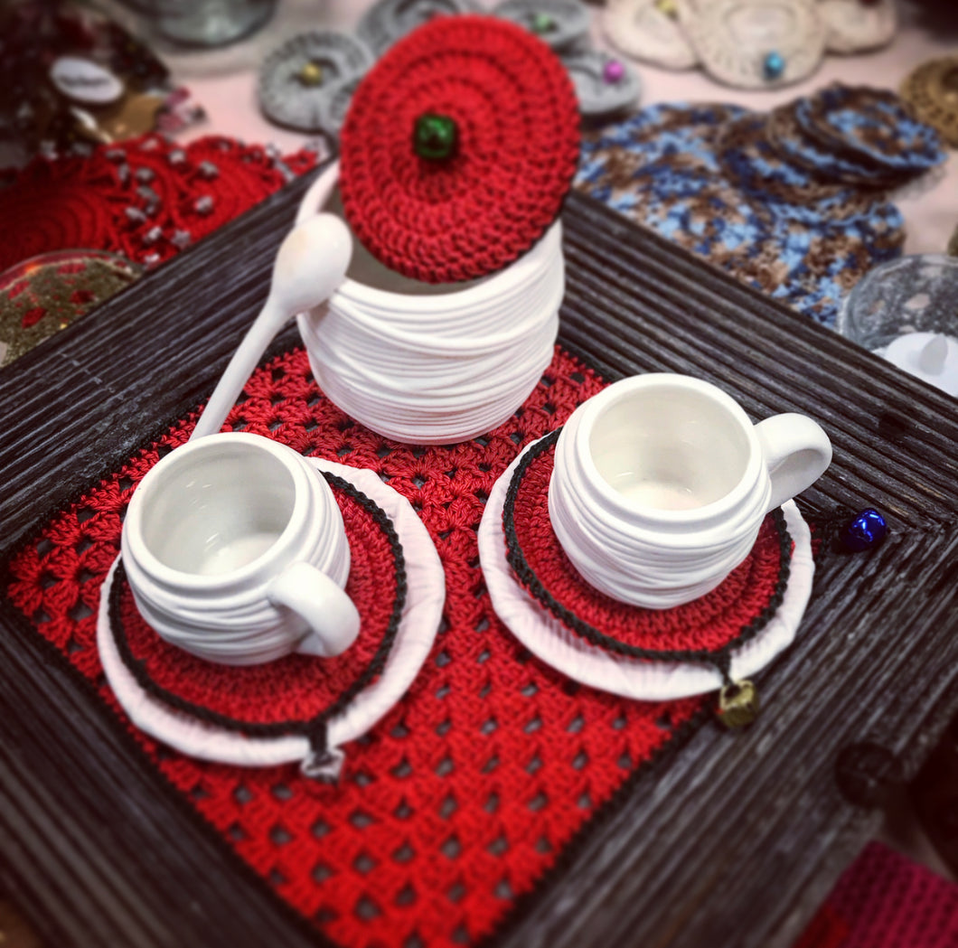 White ceramic cups with red and black coasters on a textured surface
