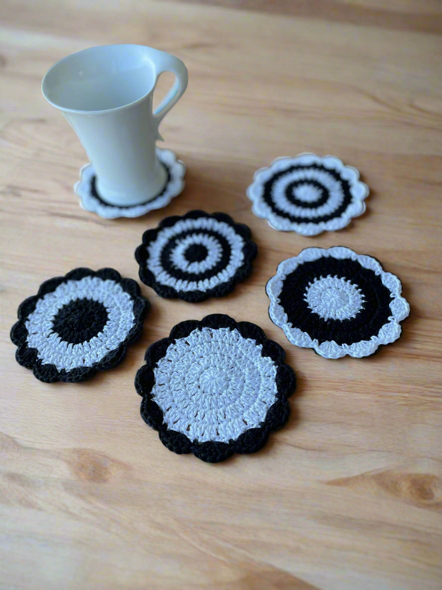 Set of black and white crochet coasters on a wooden surface with a white cup.