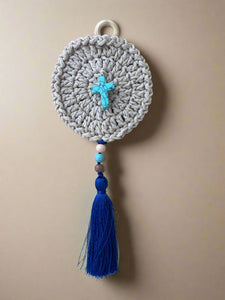 Crocheted round wall hanging with blue tassel and beads on a concrete surface