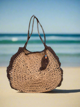 Load image into Gallery viewer, Brown crochet bag on a sandy beach with ocean in the background
