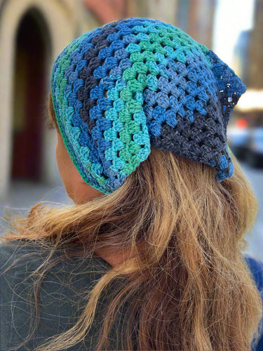 Person wearing a blue and green crocheted headband with a blurred outdoor background