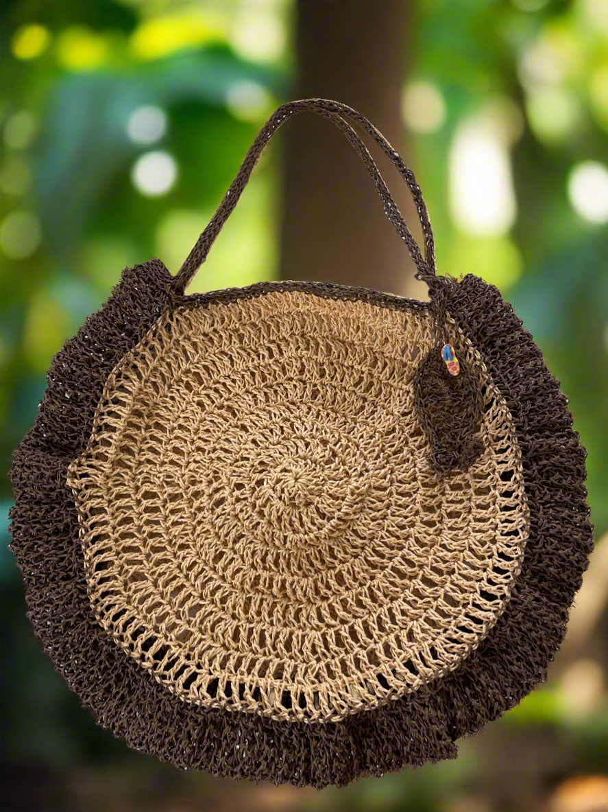 Round woven bag with brown handle against a blurred green natural background