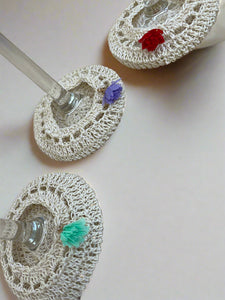 Three crocheted coasters with colorful pom-poms on a textured surface