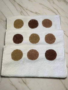 Three white towels with brown circular patterns on a beige background