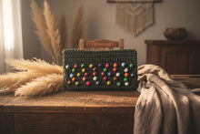 Load image into Gallery viewer, A handmade olive green crocheted clutch bag decorated with colorful wooden beads arranged in rows, set against a light marble surface.
