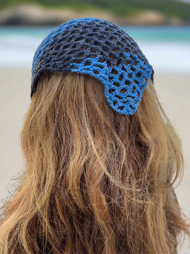 Close-up of a blue crochet headband on a person's head with a blurred outdoor background.