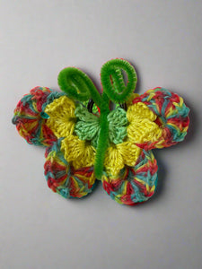 Colorful crocheted butterfly with green leaves on a textured white background