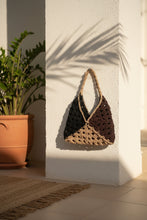 Load image into Gallery viewer, A handmade crochet shoulder bag with a dark brown and black body and a beige woven strap, draped over a weathered tree trunk outdoors.

