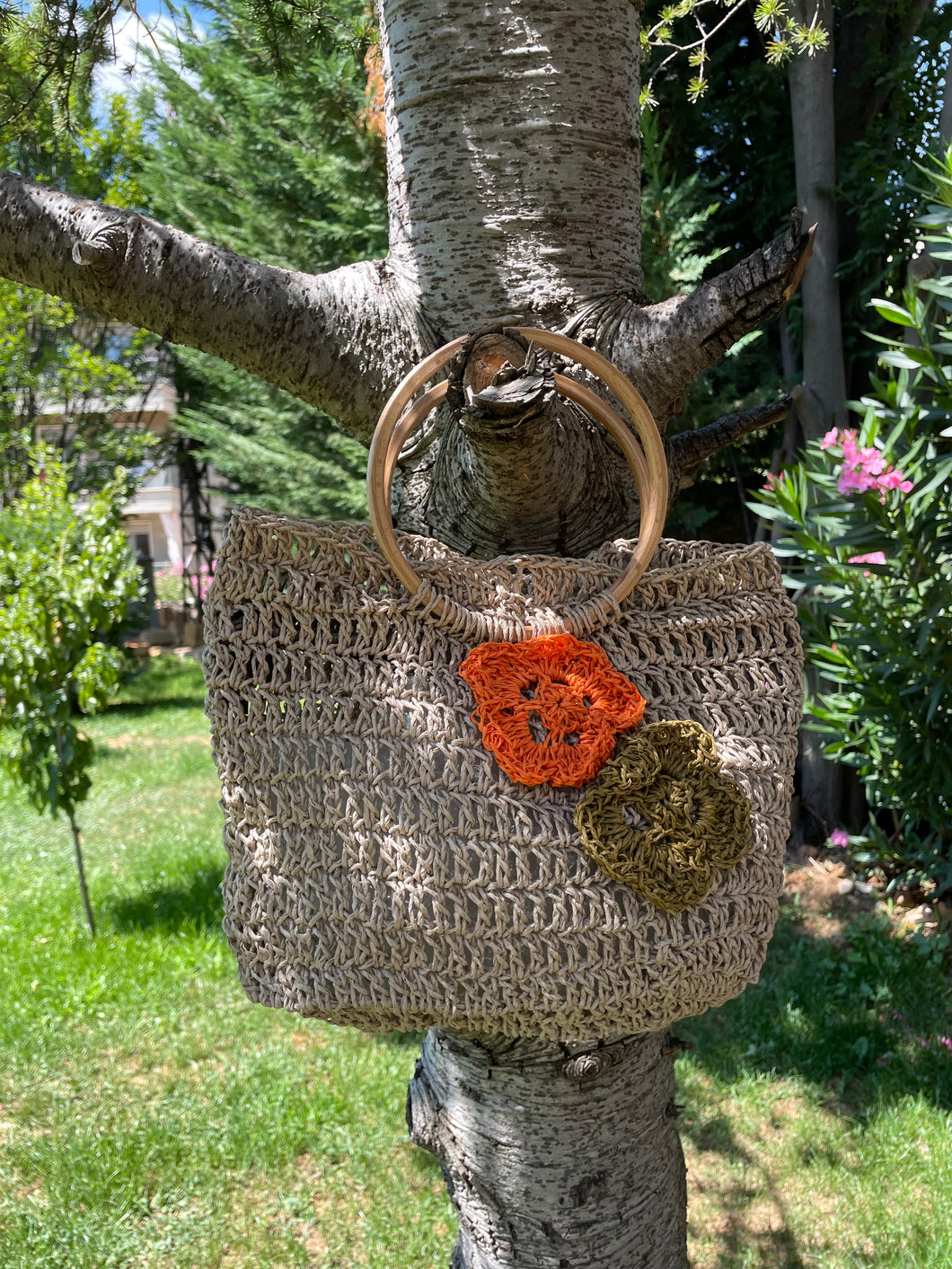 Crocheted bag with floral embellishments hanging on a tree branch