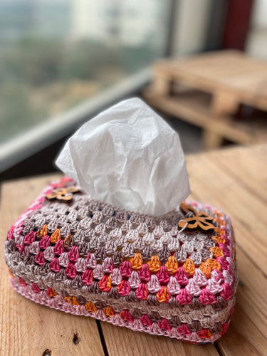Crocheted tissue box cover with tissues on a wooden surface