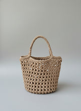 Load image into Gallery viewer, Brown crochet bag hanging on a stone wall with natural elements.
