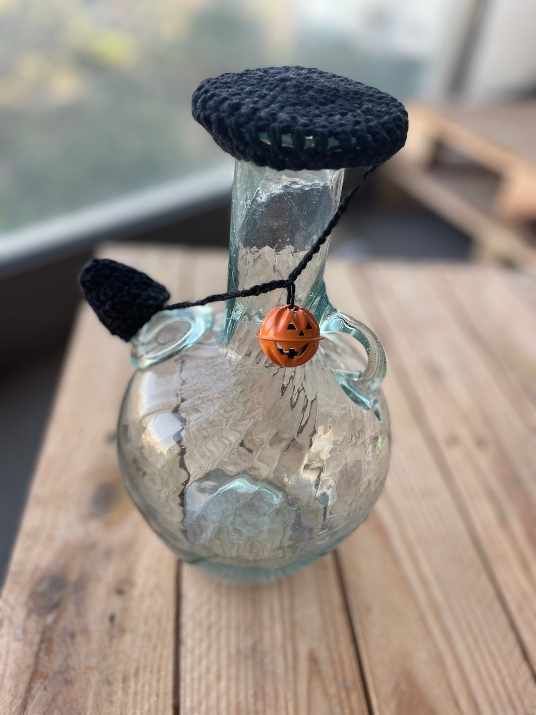 Decorative glass bottle with a black lid and small pumpkin ornament on a wooden surface.
