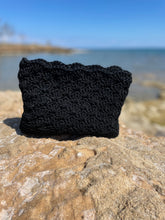 Load image into Gallery viewer, Black crochet pouch on a rock with a beach background
