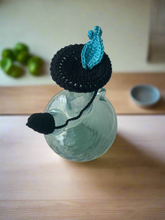 Load image into Gallery viewer, Glass bottle with a black and blue knitted cover on a wooden surface
