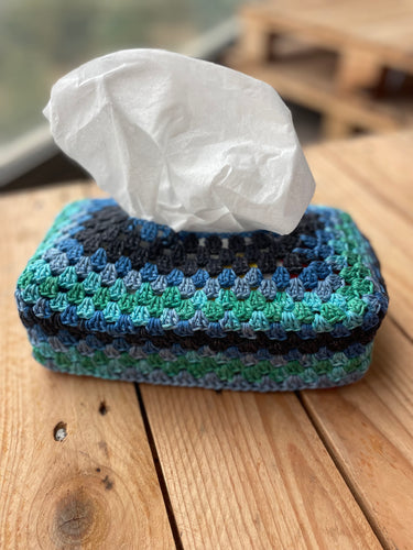 Crocheted tissue box cover with tissues on a wooden surface