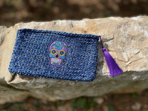 Blue woven pouch with a colorful skull design and purple tassel on a stone surface.