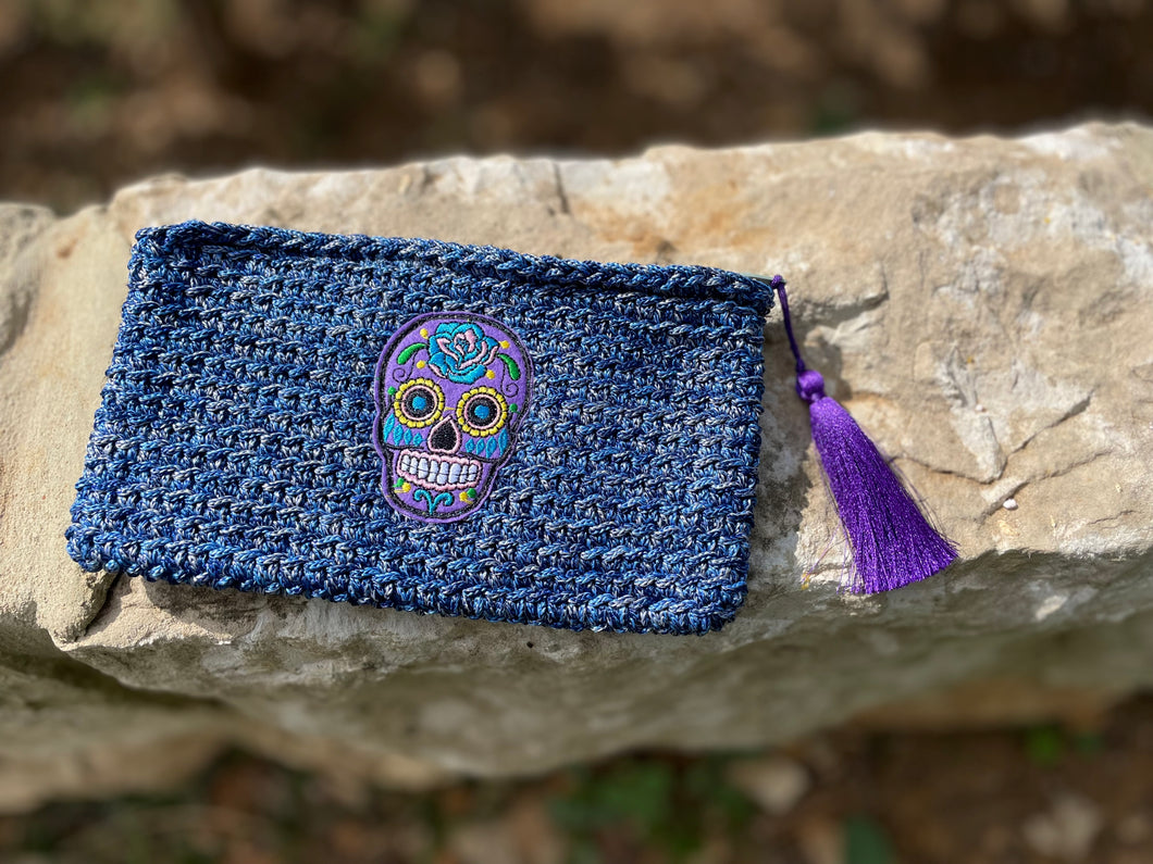Blue woven pouch with a colorful skull design and purple tassel on a stone surface.
