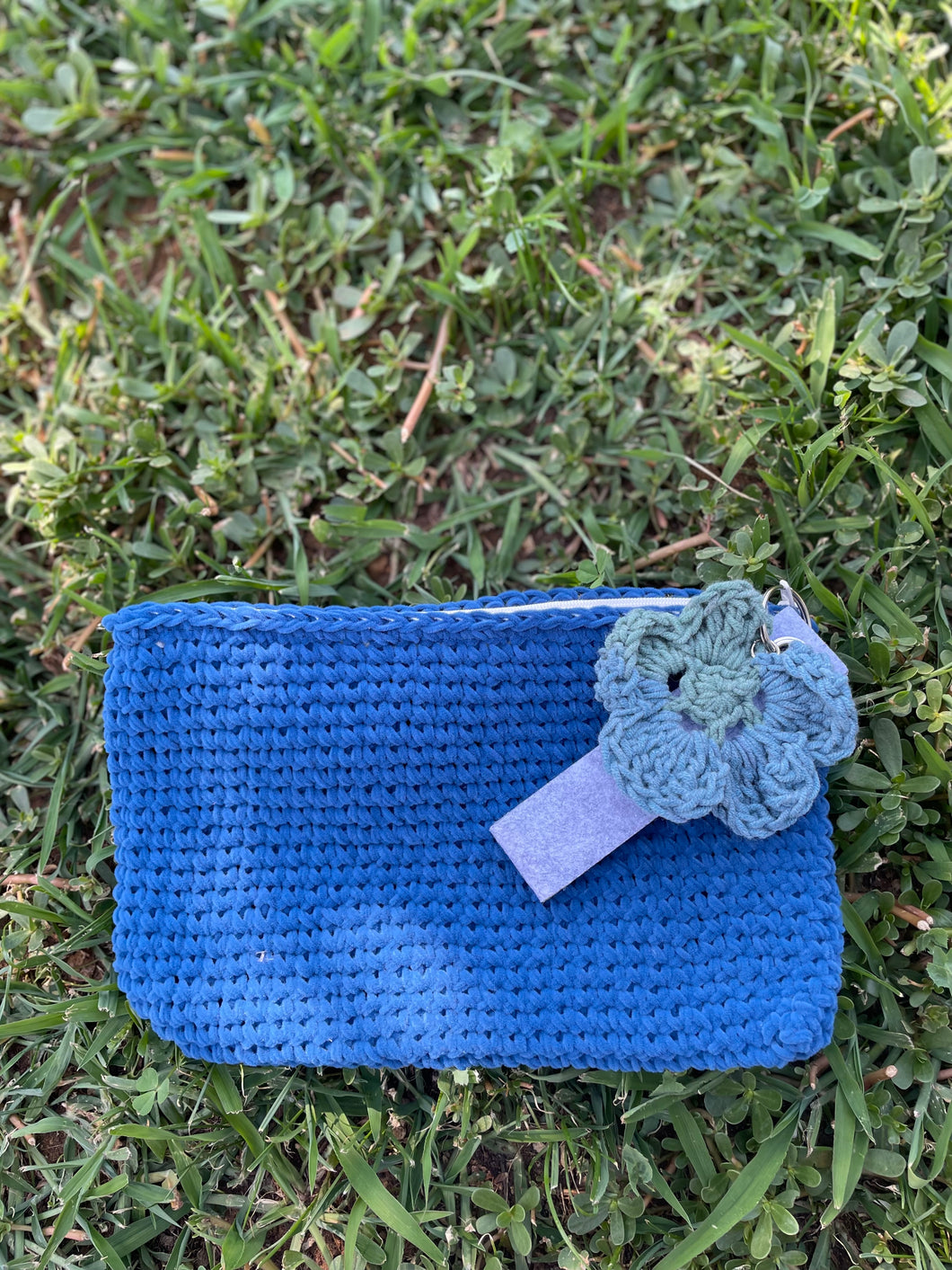 Blue crocheted pouch with a matching flower on grass