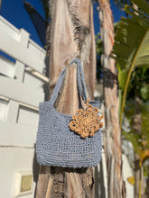 Load image into Gallery viewer, Blue crochet bag with a decorative gold piece hanging on a palm tree
