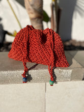 Load image into Gallery viewer, Red knitted bag with blue and green beads on a concrete surface
