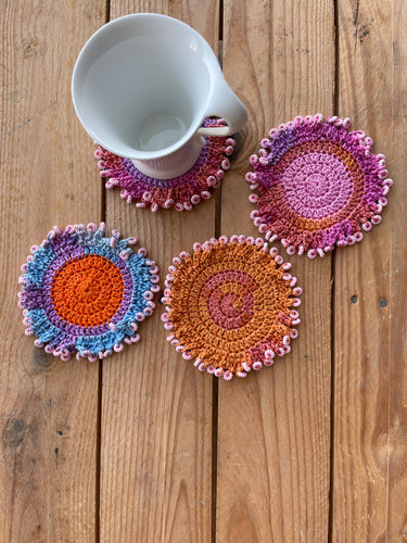 Set of colorful crocheted coasters on a wooden surface with a mug.